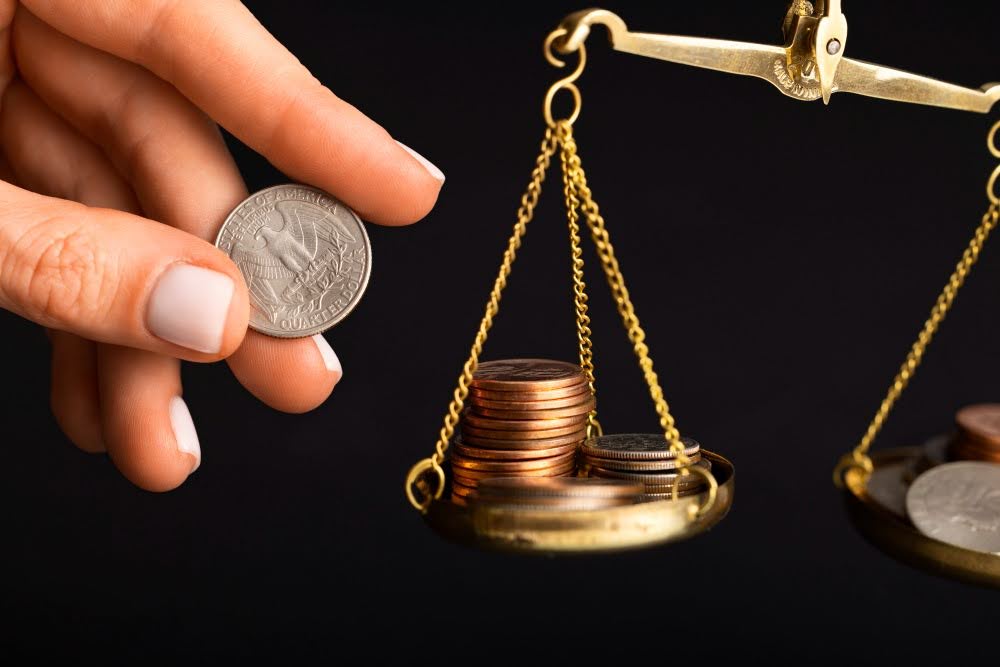 Imagem de uma balança com moedas sendo colocadas por uma pessoa